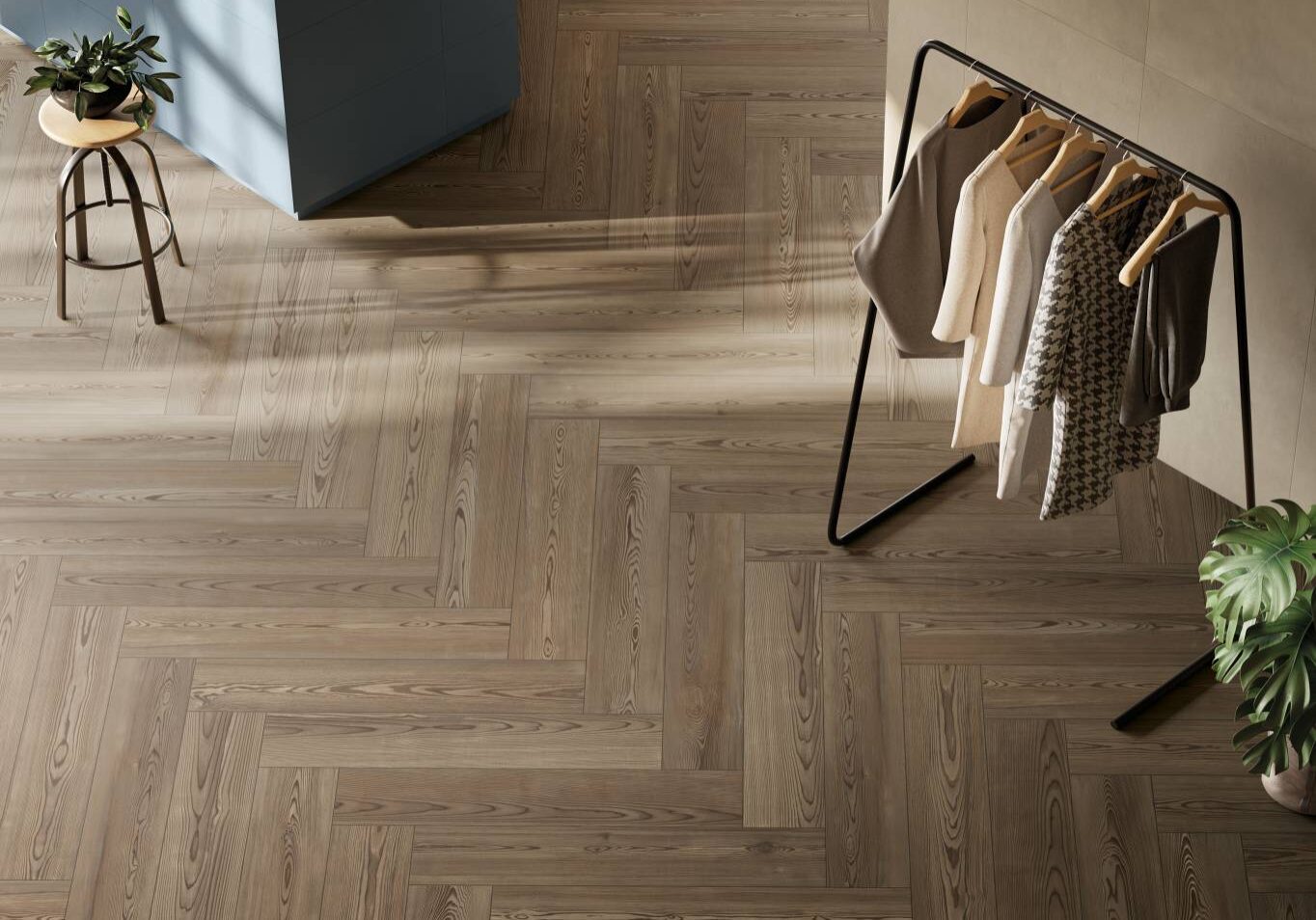 Modern room corner with herringbone wood plank floor, clothes rack and plants.