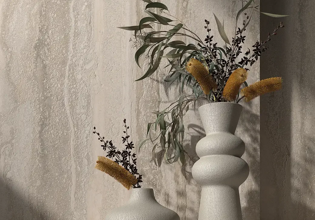 Two textured concrete vases with dried plants on a shelf against a mottled stone-effect tile wall.